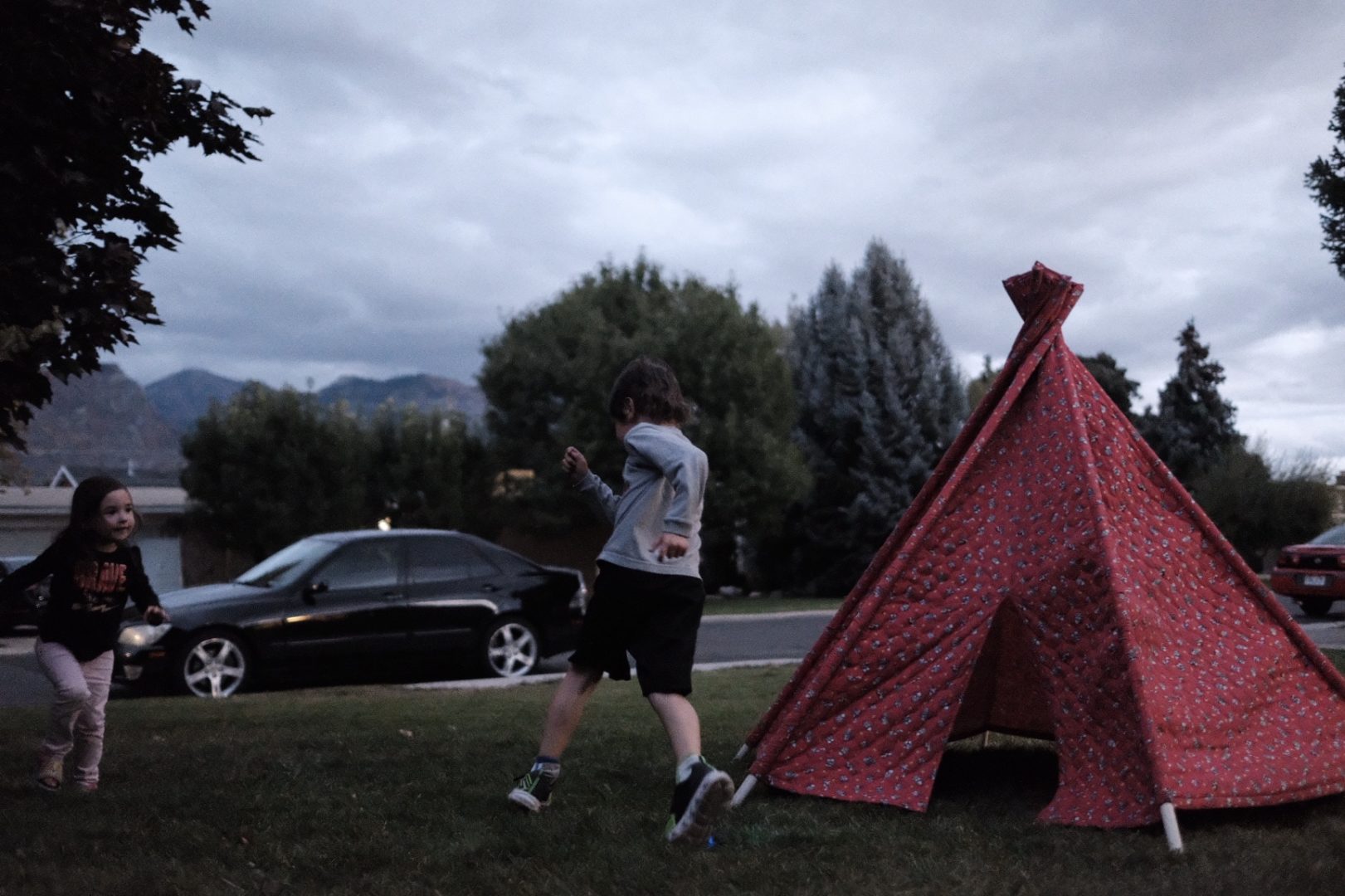 Two kids run around a teepee set up on the front lawn.